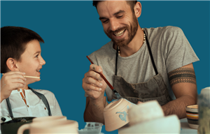 A father and son smiling and painting pottery.