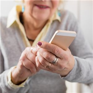 An older woman smiling while holding a cell phone in the foreground